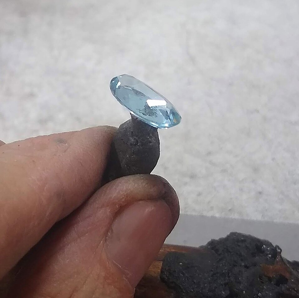 Aguamarina azul tallada sostenida sobre una herramienta de joyería
